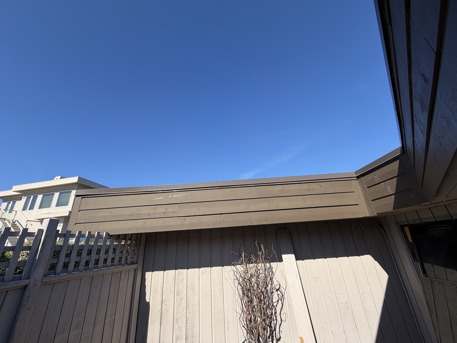 Long roof edge with metal cap flashing and dark fascia above wood siding