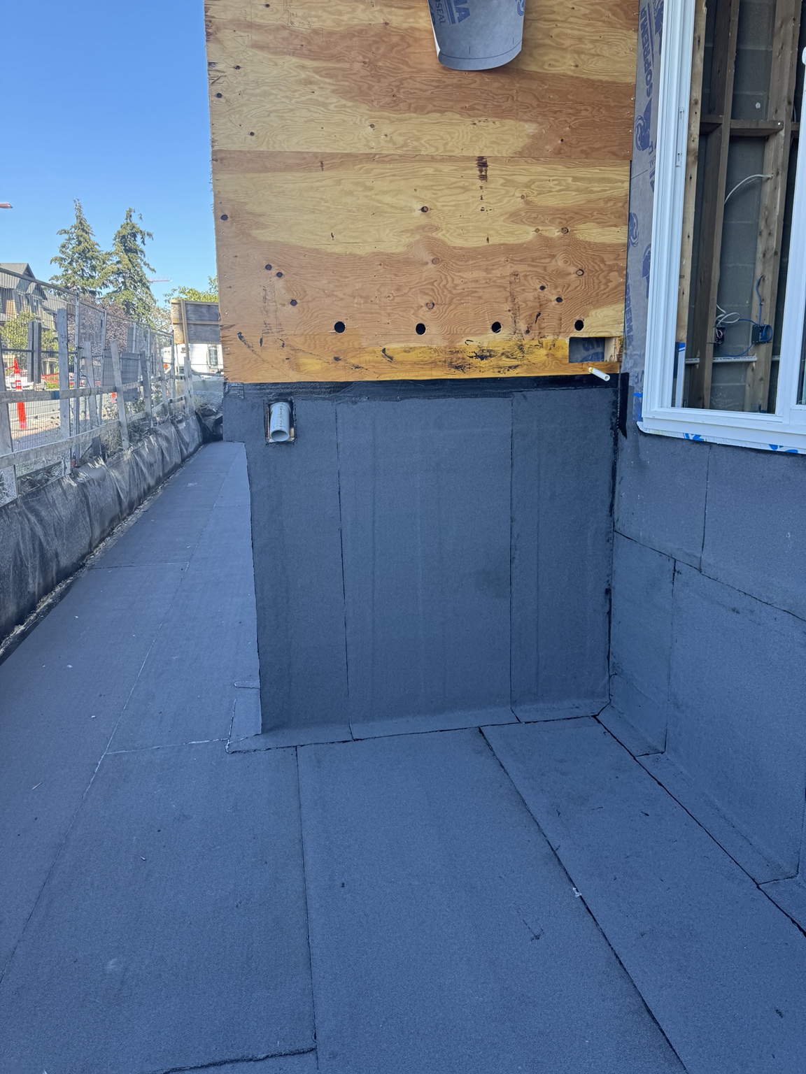 Membrane upstand and field seams at a wall base with a drain pipe, beside a window opening